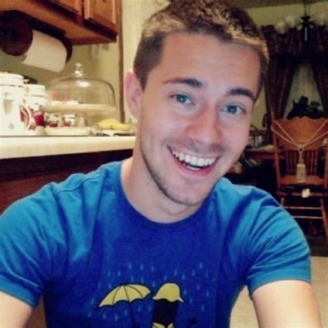 a man sitting at a table with an umbrella t shirt on smiling for the camera