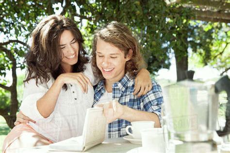 Young Couple Discussing Book At Breakfast Table Outdoors Stock Photo