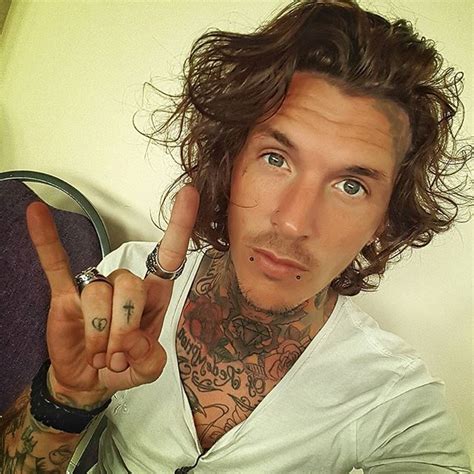 a man with long hair and tattoos holding his finger up to the side while making a peace sign