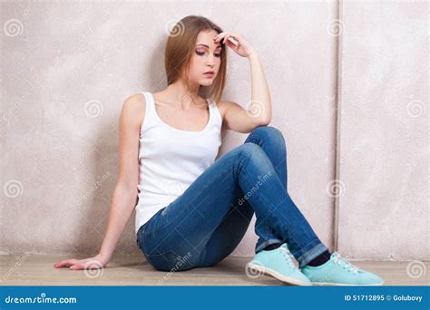 Het Nadenkende Meisje Zit Op Een Vloer Dichtbij Een Witte Muur Stock
