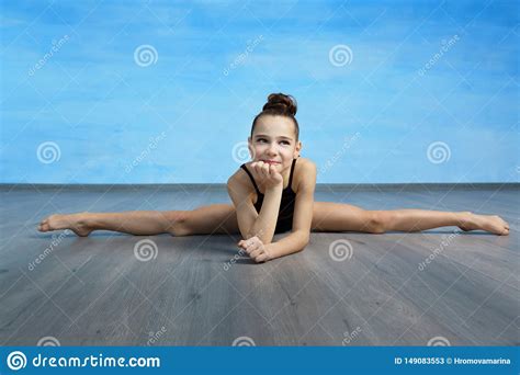 A Girl Gymnast In A Black Gymnastic Swimsuit Is Sitting On A Cross Splits On The Blue Sky