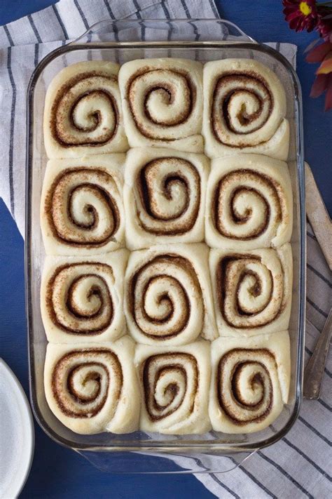 A Pan Filled With Cinnamon Rolls Sitting On Top Of A Blue Table Cloth