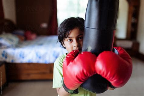 Child Wearing Boxing Gloves Holds The Punch Bag By Stocksy