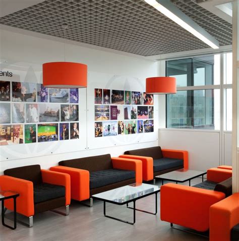 An Office With Orange And Black Couches And Pictures Hanging On The