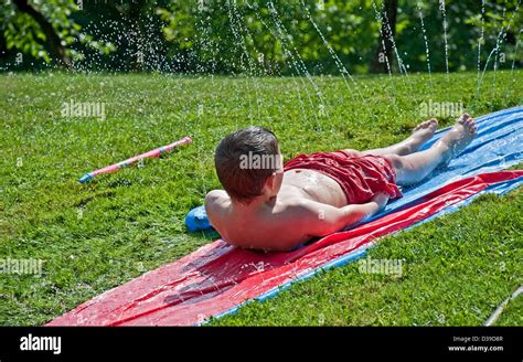 8 Year Old Caucasian Boy Is Having Summer Fun By Sliding Backwards Down A Sheet Of Plastic With