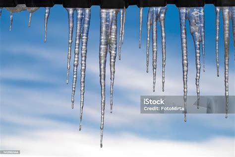 Long Icicles Hang From The Roof Against The Winter Sky Stock Photo
