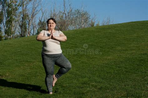 overweight middle aged woman practices yoga outdoors barefoot doing balance exercise on one leg