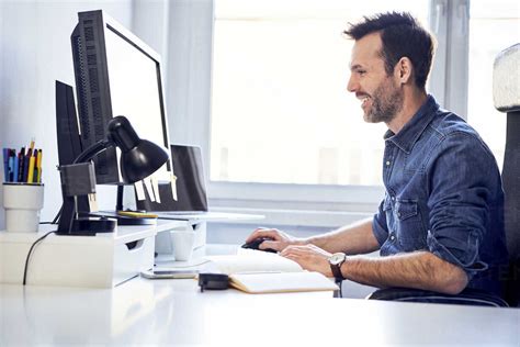 Smiling Man Working On Computer At Desk In Office Stock Photo