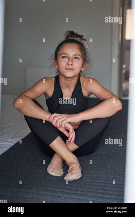 Dreamy Slim Girl In Black Sport Outfit And Gymnastic Footwear Sitting On Bed Looking Away At
