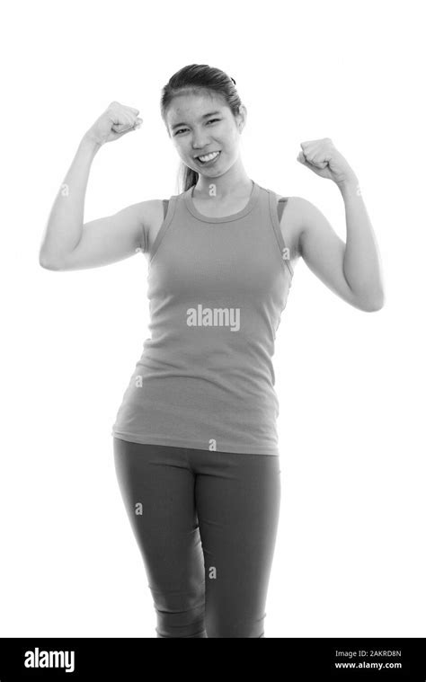 Studio Shot Of Young Happy Asian Woman Smiling While Flexing Both Arms