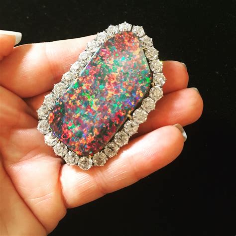A Person Holding An Opal And Diamond Brooch In Their Left Hand On A