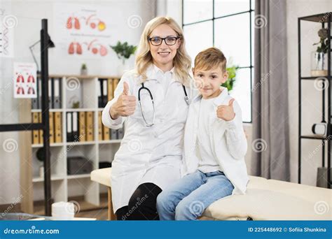 Female Doctor Hugging Her Little Male Patient And Smiling With Thumbs