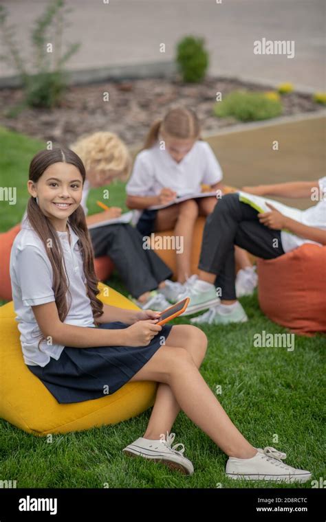 Cute Dark Haired Schoolgirl Sitting With Classmates And Smilling Stock