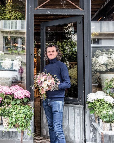 Parisian Florist Eric Chauvin Wearing In Worn Jeans And Navy Turtleneck Stands At The Open