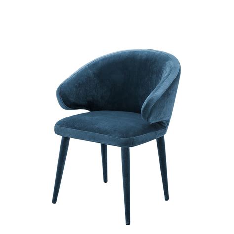 The upholstered feast chair features slender arms and tapered walnut legs for luxuriously long and comfortable dinners with friends. Cardinale Roche Teal Blue Velvet Dining Chair | SHOP NOW