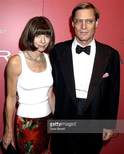 A Man And Woman Standing Next To Each Other In Front Of A Red Wall At