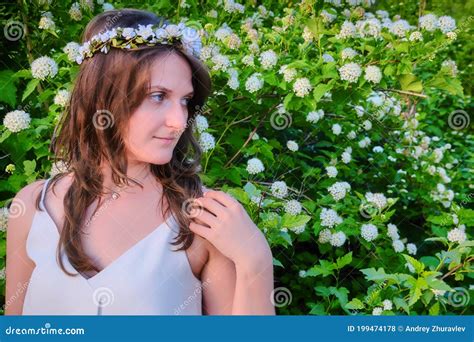 A Woman With A Wreath On Her Head Straightens Her Hair On A Background Of A Tree With Flowers