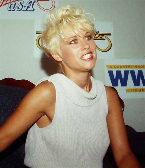 A Woman With Blonde Hair Wearing A White Top And Posing For The Camera