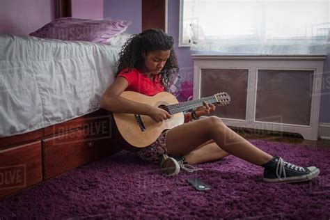 Girl Sitting On Bedroom Floor Playing Guitar Looking Down Stock Photo