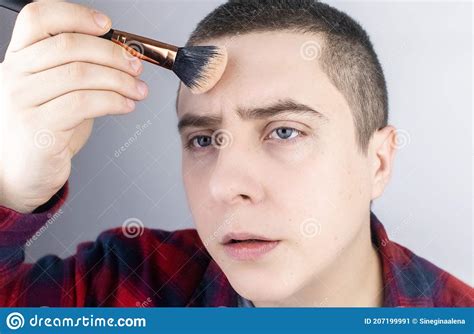 the man looks into the frame and uses powder close up of a guy putting makeup on his face lgbt