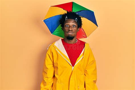 Young African American Man Wearing Yellow Raincoat Puffing Cheeks With