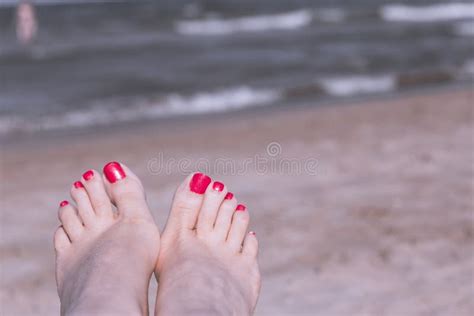 Feet Of Woman With Nails Painted Red On The Sand Of The Sea Stock Photo