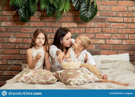Mom Sits On The Bed With Her Son And Daughter And Watch A Movie A