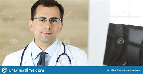Man Doctor Sitting At The Desk At His Working Place And Smiling At