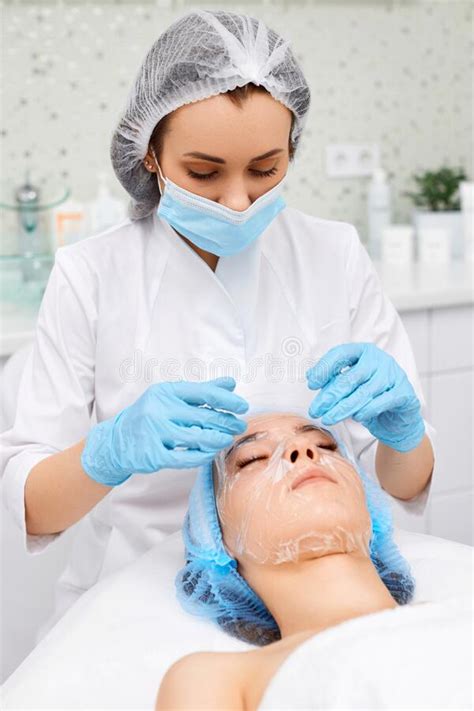 Beautician Applies The Mask To The Face Of Beautiful Woman Stock Photo