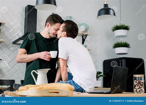 Happy Gay Couple Having Breakfast In Kitchen And Using Laptop Amorous Gay Men Kissing Each