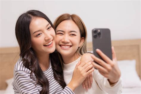 Happy Asian Couple Lesbian Video Call Talking With Friends Sitting On Sofa At Living Room Stock