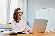 Smiling young woman working in office with laptop - Smartsys