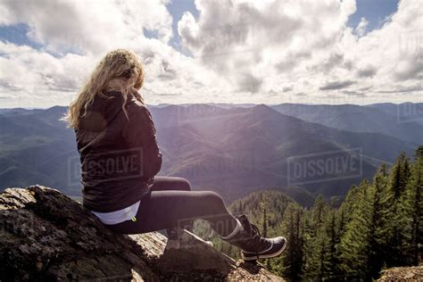 Woman Sitting On Rock At Mountain Cliff Against Cloudy Sky Stock