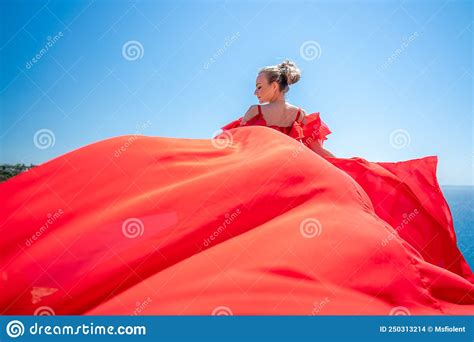Blonde With Long Hair On A Sunny Seashore In A Red Flowing Dress Back