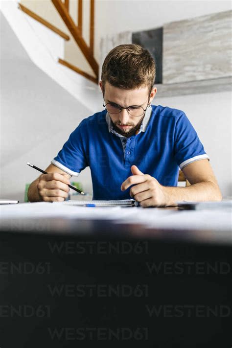 Handsome Young Man Studying While Sitting At Table Stock Photo