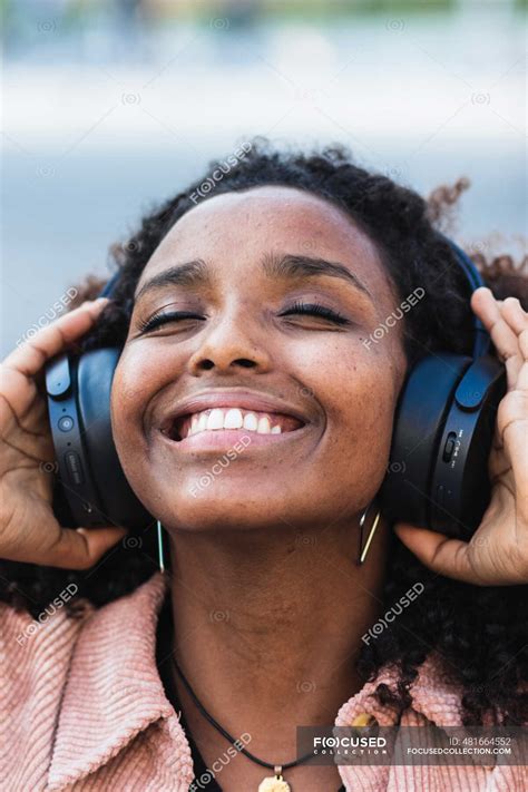 Happy Afro Woman With Eyes Closed Listening Music Through Headphones In City — Brown Hair