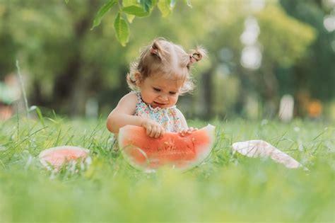 Маленькая девочка с забавной прической ест арбуз на лужайке в парке здоровая закуска для детей