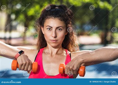 A Girl Athlete Performs Exercises With Dumbbells On A Sports Ground In