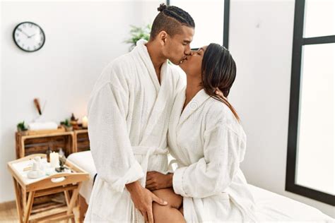 Young Latin Couple Wearing Bathrobe Kissing And Sitting On Massage