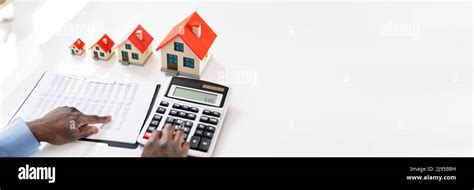 Businessman Calculating Tax By Small And Big House Models Stock Photo