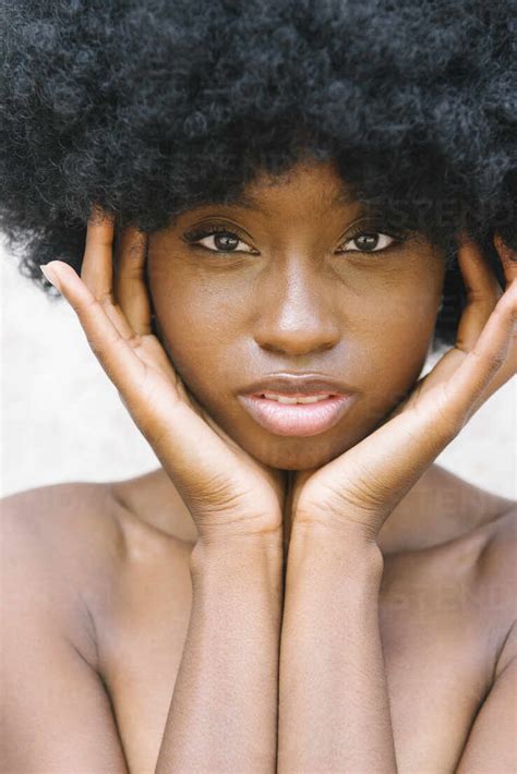 Young African American Female Model With Curly Hair Touching Face And Covering Naked Breast With