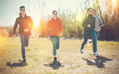 Happy Teenage Friends Chasing Each Other On Green Meadow Stock Photo