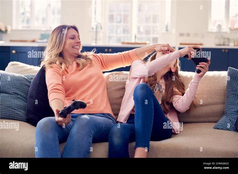 Mother Cheating As She And Daughter Have Fun Sitting On Sofa At Home Playing On Games Console