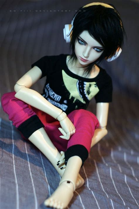A Doll With Headphones Sitting On A Bed Wearing Pink Pants And A Black