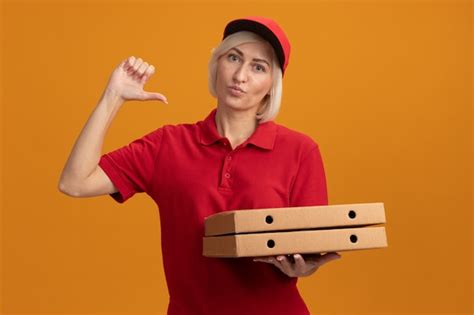Free Photo Confident Middle Aged Blonde Delivery Woman In Red Uniform And Cap Holding Pizza