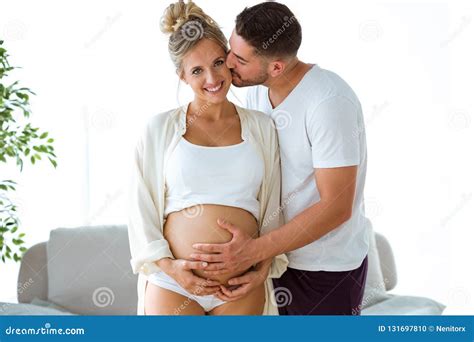 Handsome Young Man Touching Belly Of Beautiful Pregnant Woman While Man Kissing To His Wife At