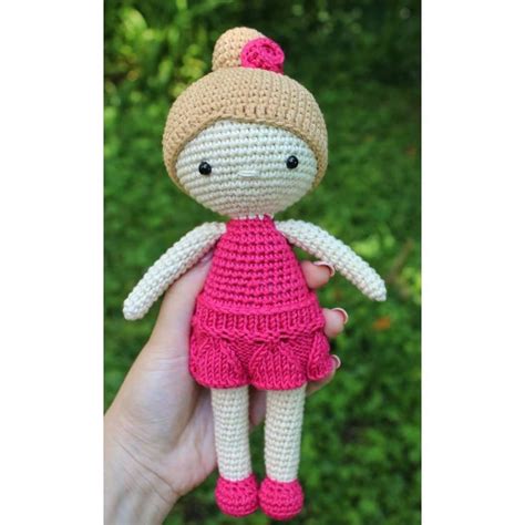 A Small Crocheted Doll In A Pink Dress Is Held By Someones Hand