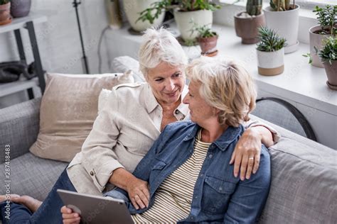 Mature Lesbian Couple Looking At Digital Tablet Together On Sofa Foto