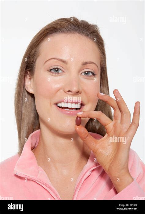 Female Fair Hair Off Her Face Wearing A Pink Jacket Holding A Multivitamin Tablet Between Her