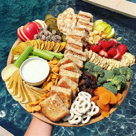 A Platter With Fruit Vegetables And Crackers Next To A Swimming Pool